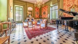 Una sala amplia con un piano, sillas ornamentadas, un candelabro y un tapete con diseños.