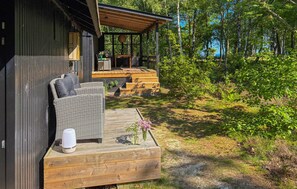 A wooden deck with wicker furniture and a glass table, surrounded by a forested area.