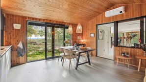 Un intérieur moderne avec des murs en bois, un coin repas comprenant une table et des chaises, et de grandes fenêtres offrant une vue sur l’extérieur.