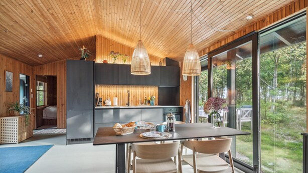 Une cuisine moderne avec un lambris en bois, un coin repas avec deux chaises et une grande fenêtre donnant sur une forêt.