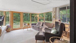 Un salon moderne avec une grande fenêtre, un canapé, un fauteuil et une petite table sur laquelle se trouve un panier.