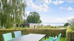 A patio with a table and chairs, overlooking a body of water and a building with a modern design. - Nice apartment in Egernsund with WiFi (Egernsund)