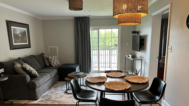 A modern living room with a dark grey sofa, a dining table with four chairs, and a large window with curtains. - Golf Getaway, 5 miles to Pinehurst (Carthage)