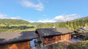 Une cabane en rondins dotée d’un patio, entourée de collines boisées et surplombant un ciel dégagé.