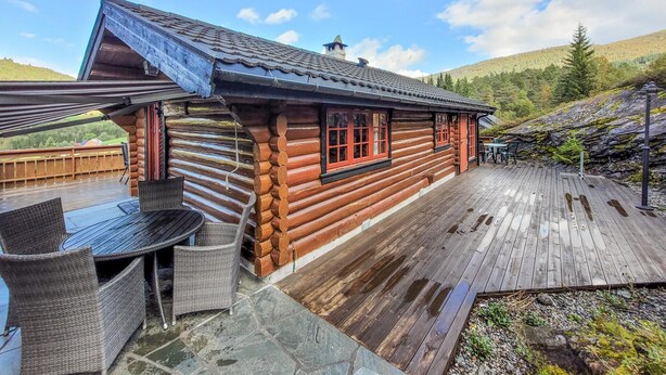 Une cabane en rondins avec une terrasse en bois, du mobilier d’extérieur et une vue sur les montagnes en toile de fond.