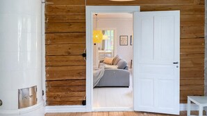A wooden interior with a white door leading to a room with a bed, a lamp, and a small table.