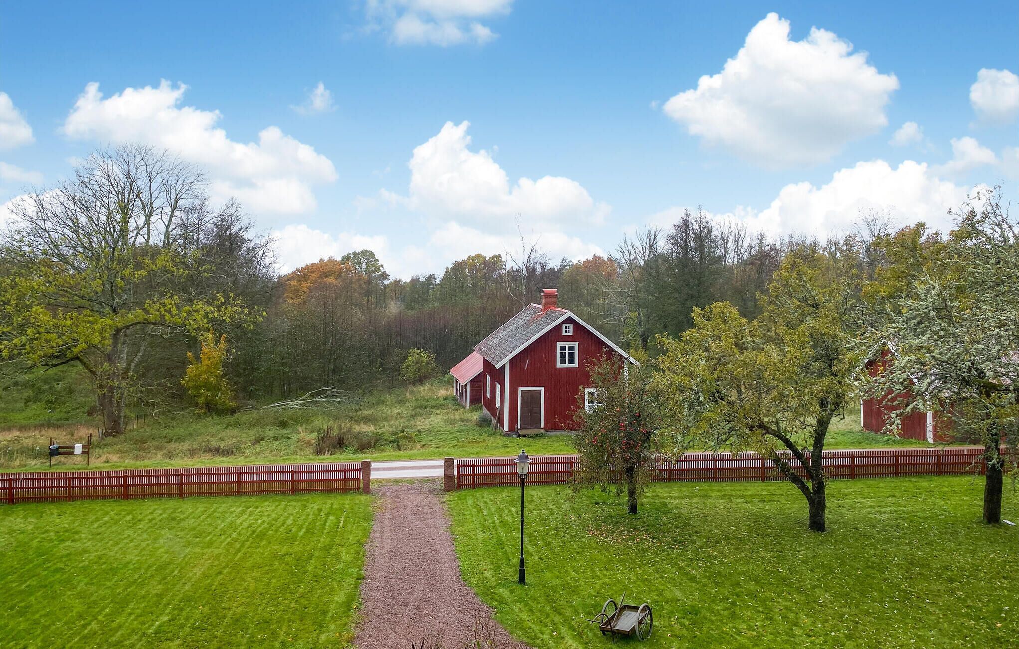 A red barn with a gravel path leading to it, surrounded by green grass and trees.