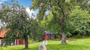 A rustic cabin with a red exterior, surrounded by lush greenery and trees.