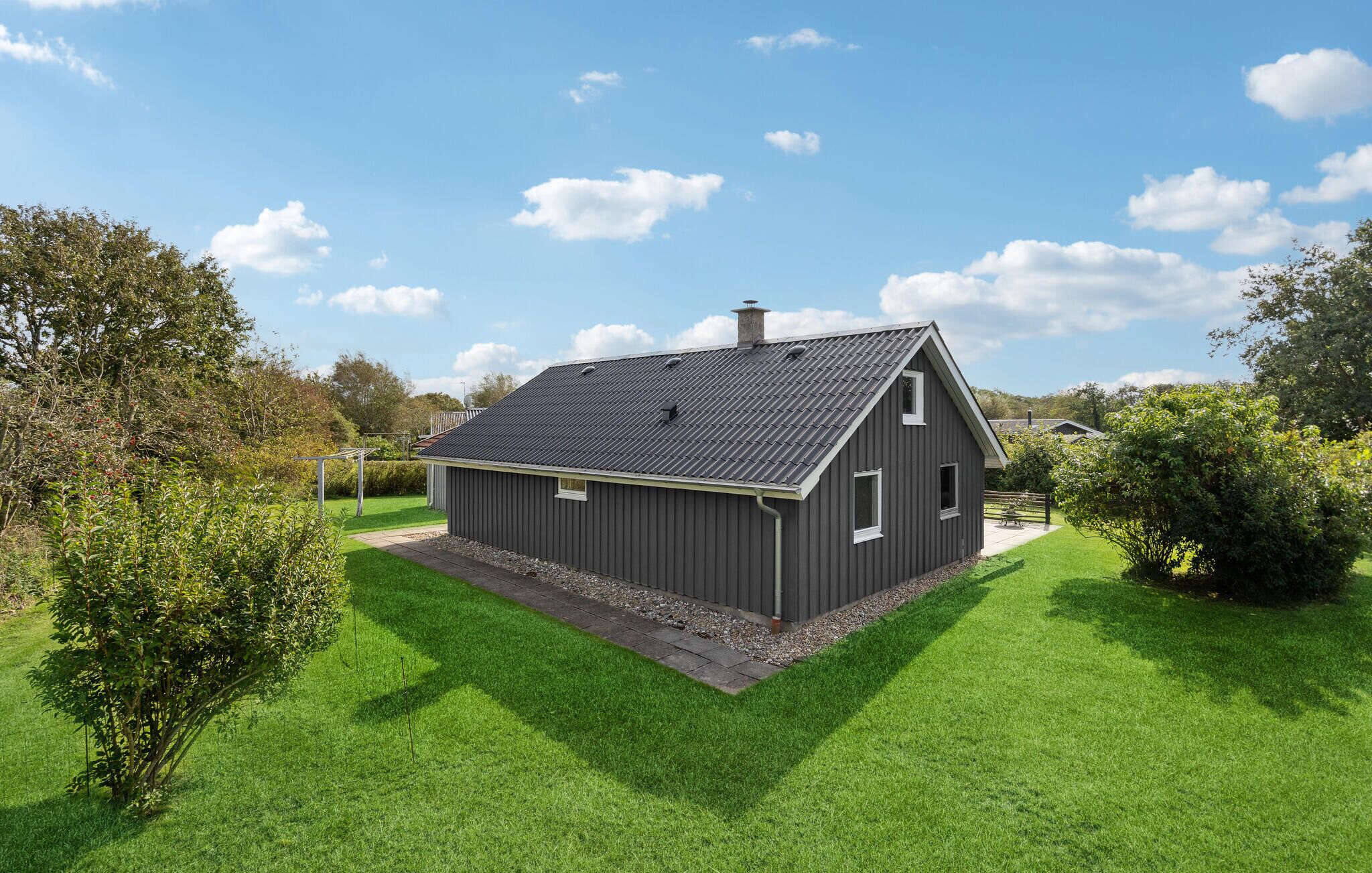 A single-story, dark-colored building with a sloped roof, surrounded by well-maintained green grass and trees.