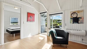 A spacious room with a wooden floor, a black sofa, a red artwork, and a window with a view of greenery.