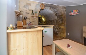 Compact kitchen with a wooden countertop, small refrigerator, and stone wall.