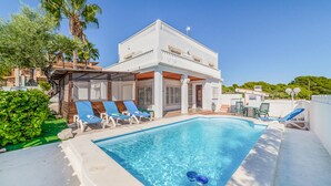Un espace aménagé au bord d’une piscine à l’eau d’un bleu limpide, avec un bâtiment blanc doté de balcons et des chaises longues vertes.