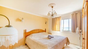Une chambre à coucher avec un lit en bois, un lustre, une fenêtre avec des rideaux et un ventilateur.