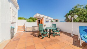 Une terrasse avec une table et des chaises, une vue sur la mer et un bâtiment orné d’une enseigne représentant un voilier.