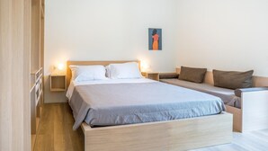 Une chambre à coucher comprenant un lit, des tables de chevet, un canapé et une œuvre d’art accrochée au mur.