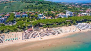 Vue aérienne d’une ville côtière, avec une plage bordée de nombreux parasols et de chaises longues.