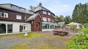 Un bâtiment en bois doté d’une véranda en verre, d’un espace extérieur aménagé pour s’asseoir et d’une fontaine.