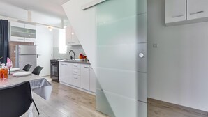 A modern kitchen with white cabinetry, a dining area with a table set for two, and a staircase with a glass panel.