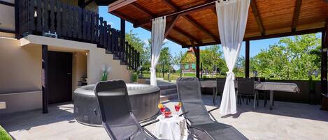 An outdoor patio with lounge chairs, a hot tub, and a covered dining area with a view of the surrounding landscape.