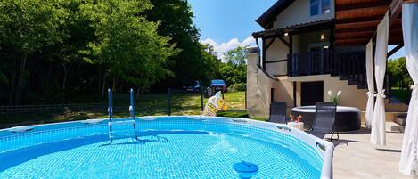 A swimming pool with a tiled deck, a lounge area with chairs and a table, and a building with a balcony.