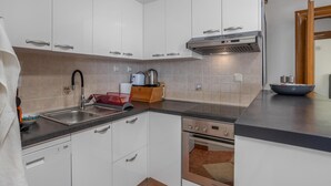 A modern kitchen with white cabinets, a stainless steel sink, a built-in oven, and a range hood.