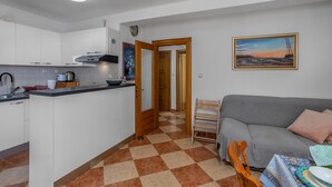 A compact living space with a kitchenette, a gray sofa, a wooden chair, and a checkered floor.