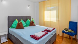 A neatly made bed with colorful pillows, a blue chair, and a wooden floor.