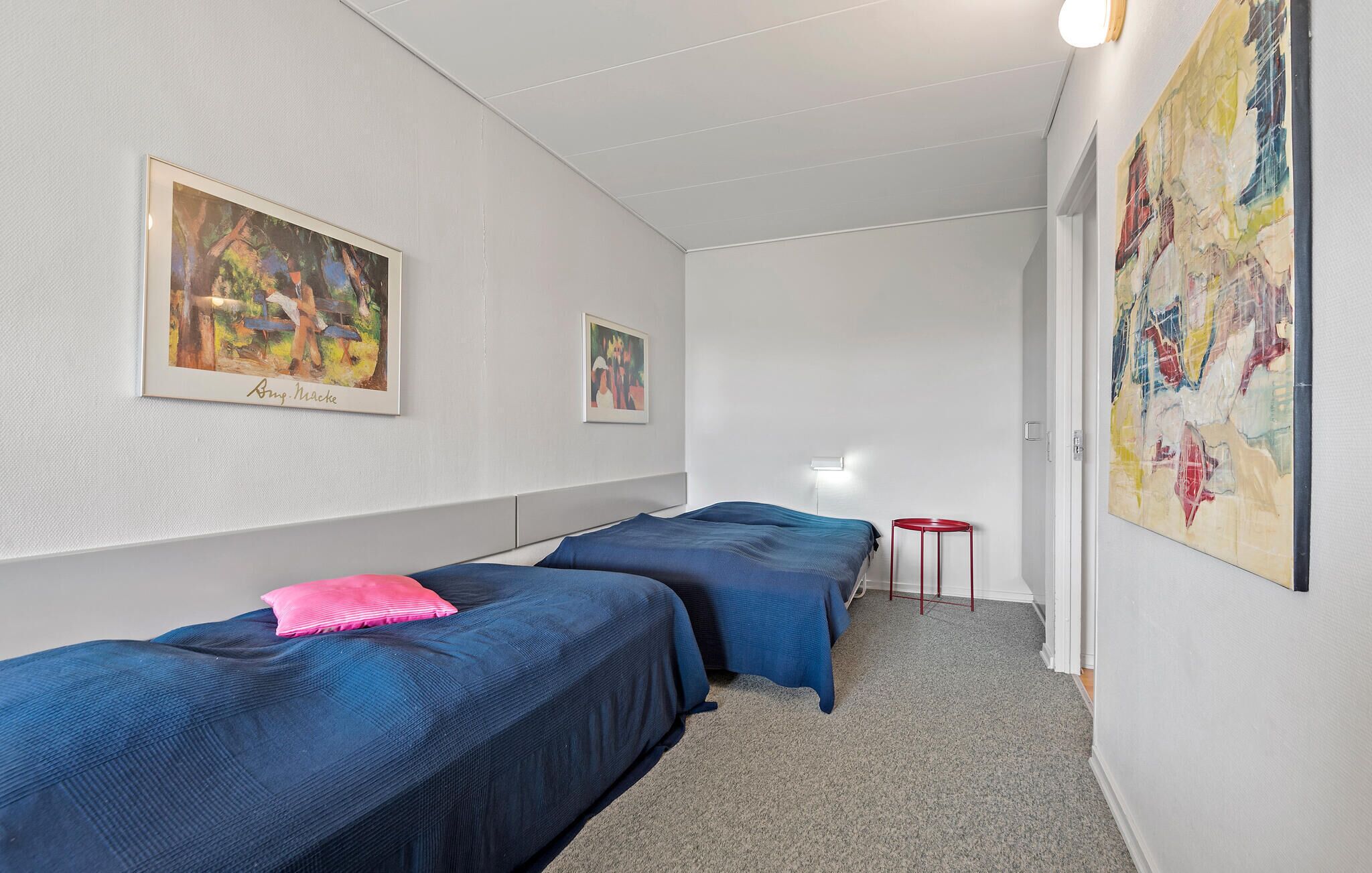 Ein Zimmer mit zwei Betten, einem kleinen Tisch und zwei Bildern an den Wänden.