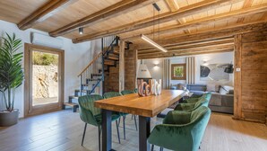 Ein geräumiger Raum mit Holzboden, einem Esstisch mit Stühlen, einer Treppe und einer Sitzecke mit Sofa und Gemälde.