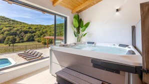 Ein moderner Wellnessbereich mit Whirlpool, Holzterrasse und Blick auf eine Berglandschaft.