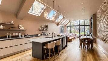 A modern kitchen with a central island, pendant lighting, and a view of the outdoors through large windows.
