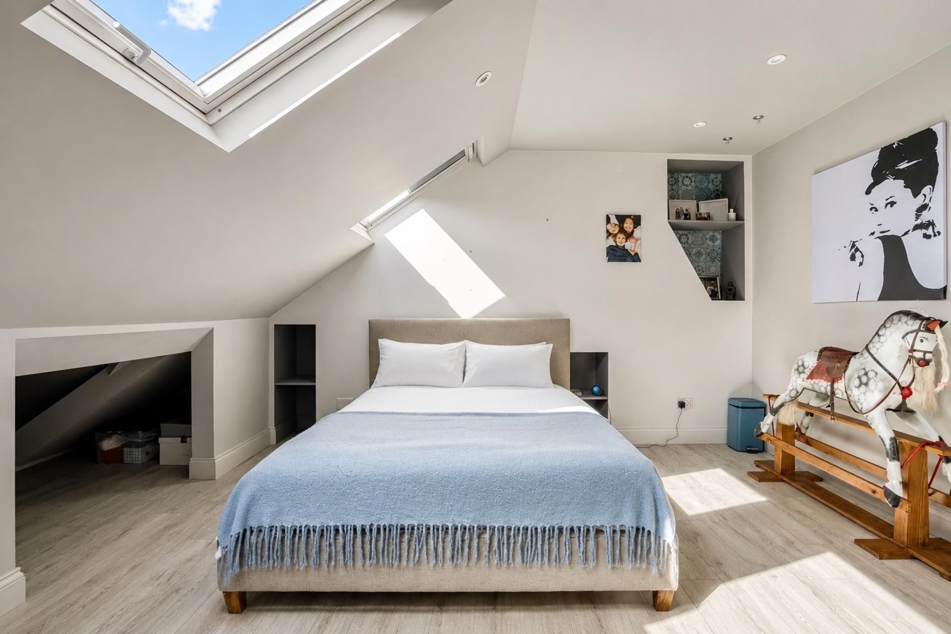 Une chambre à coucher avec un puits de lumière, un lit, une table de chevet, une commode et un mur décoré d’œuvres d’art.