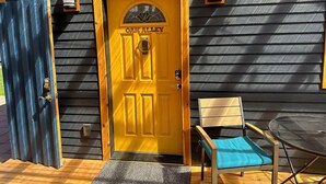 Une porte jaune avec l’inscription « OAK ALLEY » au-dessus, une porte bleue à gauche, et une petite table avec un coussin bleu sur le porche.