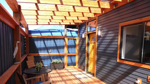 Une terrasse en bois avec une table et des chaises, un pot de fleurs et une porte portant l’inscription « BRise MARINE ».