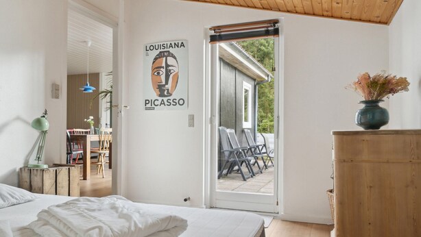 Un dormitorio con cama, una puerta con un cartel, un aparador de madera y vista al patio exterior.