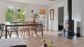 Una sala de estar moderna con una estufa de leña negra grande, muebles de madera y ventanas amplias que dan a zonas verdes.