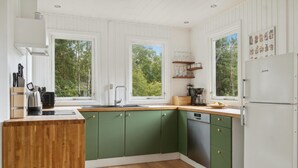 Una cocina con armarios verdes, encimera de madera, fregadero, cafetera y refrigerador.