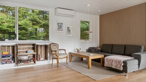 Una sala de estar con suelo de madera, un sofá gris, una mesa de centro de madera, un sillón estampado y una estantería llena de juegos de mesa.