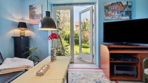 A living room with a TV, a lamp, a table with a vase, and a view of the outside. - 2 bedroom amazing apartment in Allinge (Allinge)