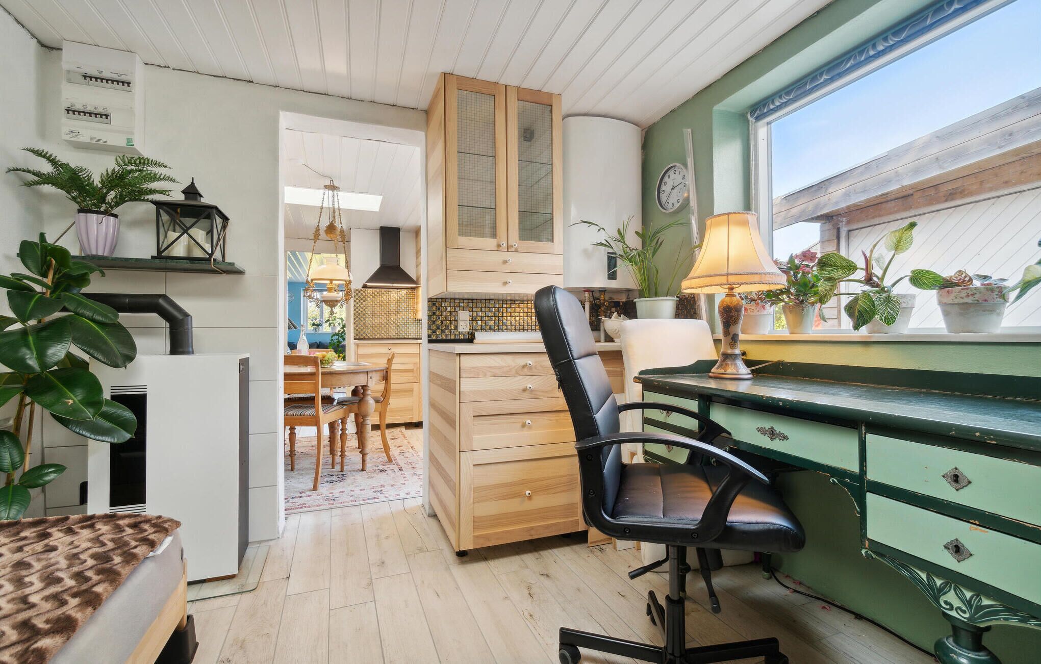 Une cuisine chaleureuse avec des meubles en bois, un coin repas comprenant une table et des chaises, et une fenêtre ornée de plantes sur le rebord.