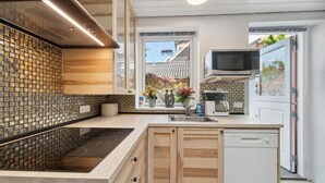 A modern kitchen with a built-in stove, a microwave, and a dishwasher. There is a window with a view of a house and trees. - 2 bedroom amazing apartment in Allinge (Allinge)