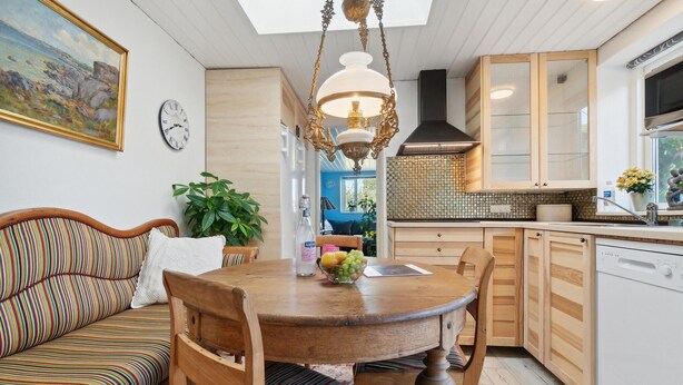 A cozy kitchen with a wooden dining table, a sofa with striped cushions, and a hanging light fixture. - 2 bedroom amazing apartment in Allinge (Allinge)
