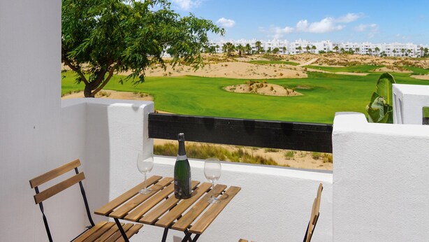 Un balcon donnant sur un terrain de golf, une bouteille de vin et deux verres posés sur une table en bois.