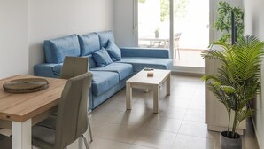 Un salon moderne avec un canapé bleu, une table basse en bois et une table à manger avec des chaises. Une grande fenêtre offre une vue sur l’extérieur.