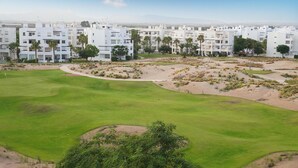 Un parcours de golf situé dans un paysage désertique, entouré d’immeubles d’habitation blancs.