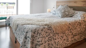 Un lit avec une couette à motifs floraux, un plaid blanc moelleux et un coussin gris à fleurs.