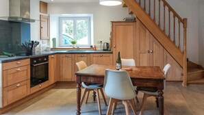 Une cuisine avec des meubles en bois, une table à manger et des chaises. Une fenêtre offre une vue sur la verdure à l’extérieur.