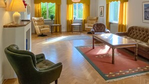A living room with a sofa, armchairs, a coffee table, and a rug. There are windows with yellow curtains, a lamp, and a radiator. - 6 bedroom gorgeous home in Tranås (Tranås)