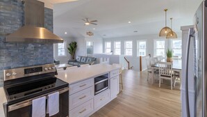 A modern kitchen with a large island, stainless steel appliances, and a stone backsplash. - 🏖️1 min to beach access!🏊  ‍♂️Heated pool, hot tub, pets, ocean views, arcade! (Nags Head)