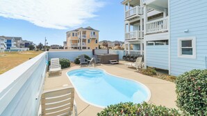 A residential area with a swimming pool, outdoor seating, and multi-story buildings. - 🏖️1 min to beach access!🏊‍♂️Heated pool, hot tub, pets, ocean views, arcade! (Nags Head)